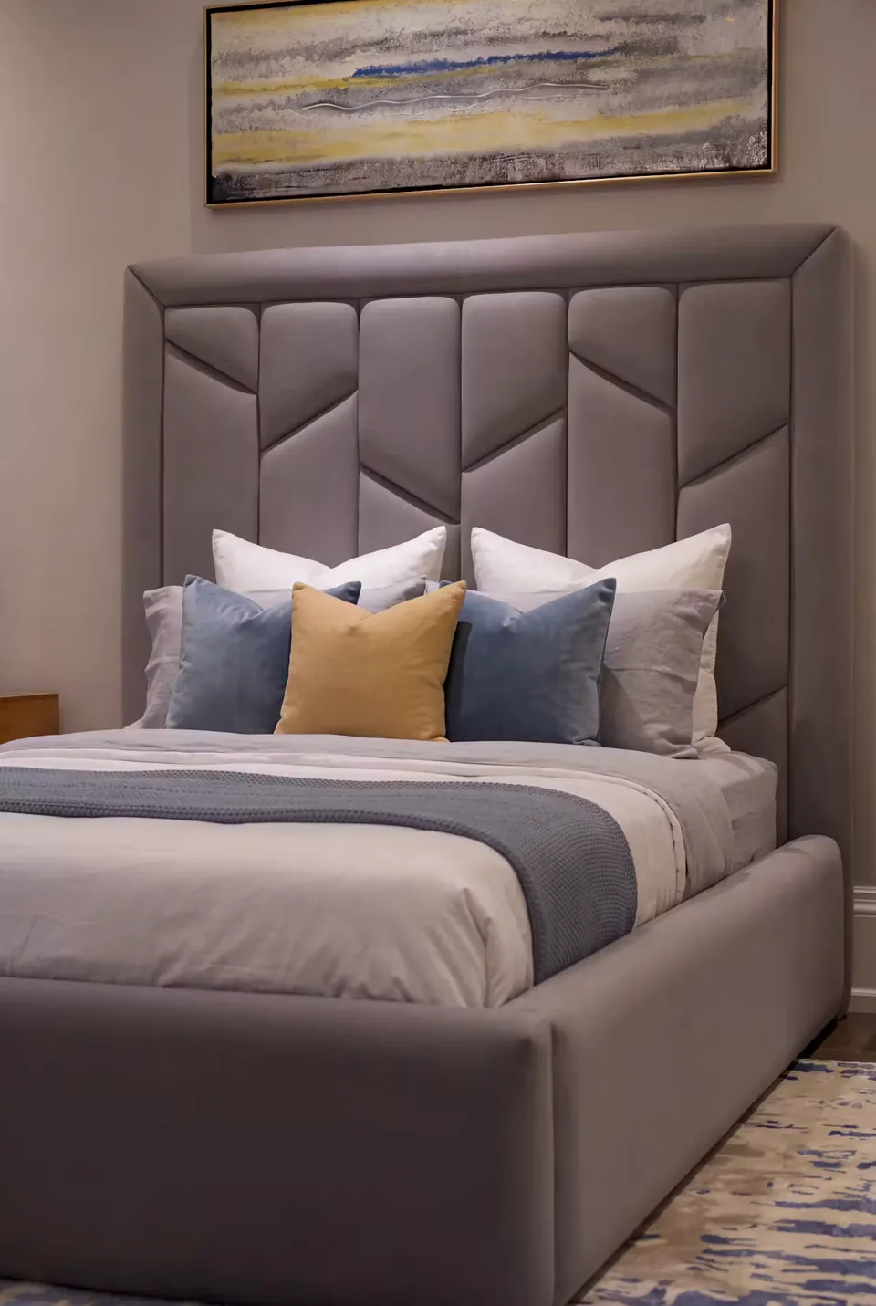 Detail of the grey faceted headboard, blue pillows and smooth upholstered frame.