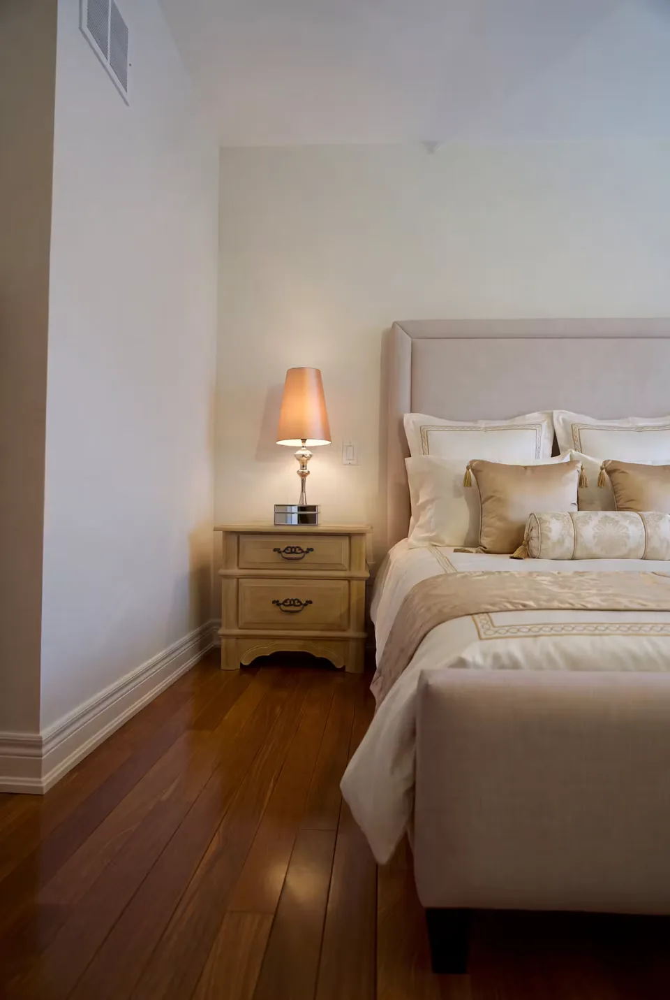 Front corner of the grey bed with neutral pillows and warm wood flooring