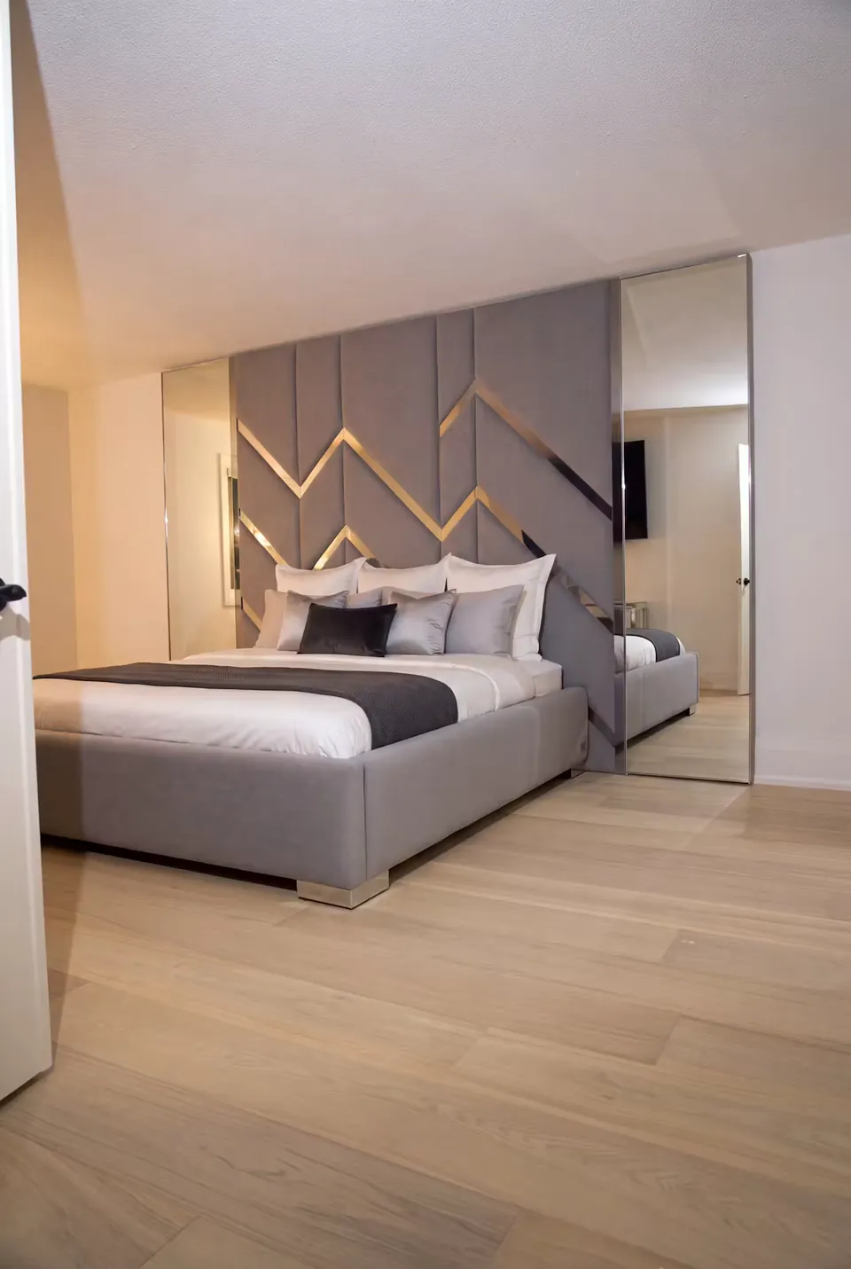Wide view of the grey bed and mirrored geometric headboard wall.