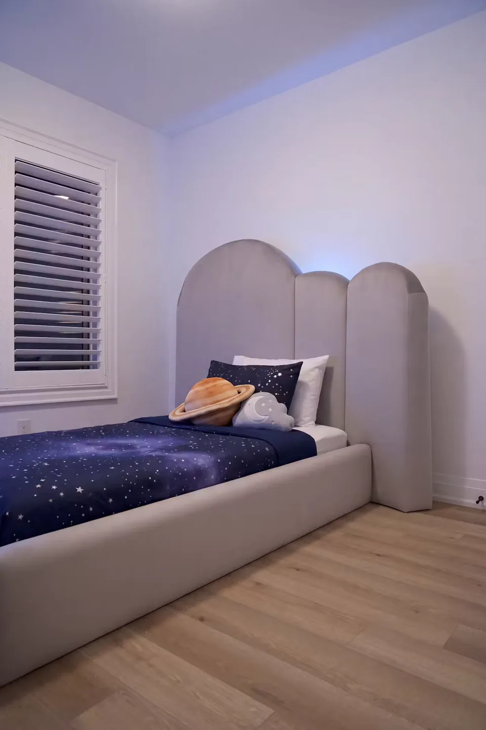 Angled view of the grey bed and stepped rounded headboard