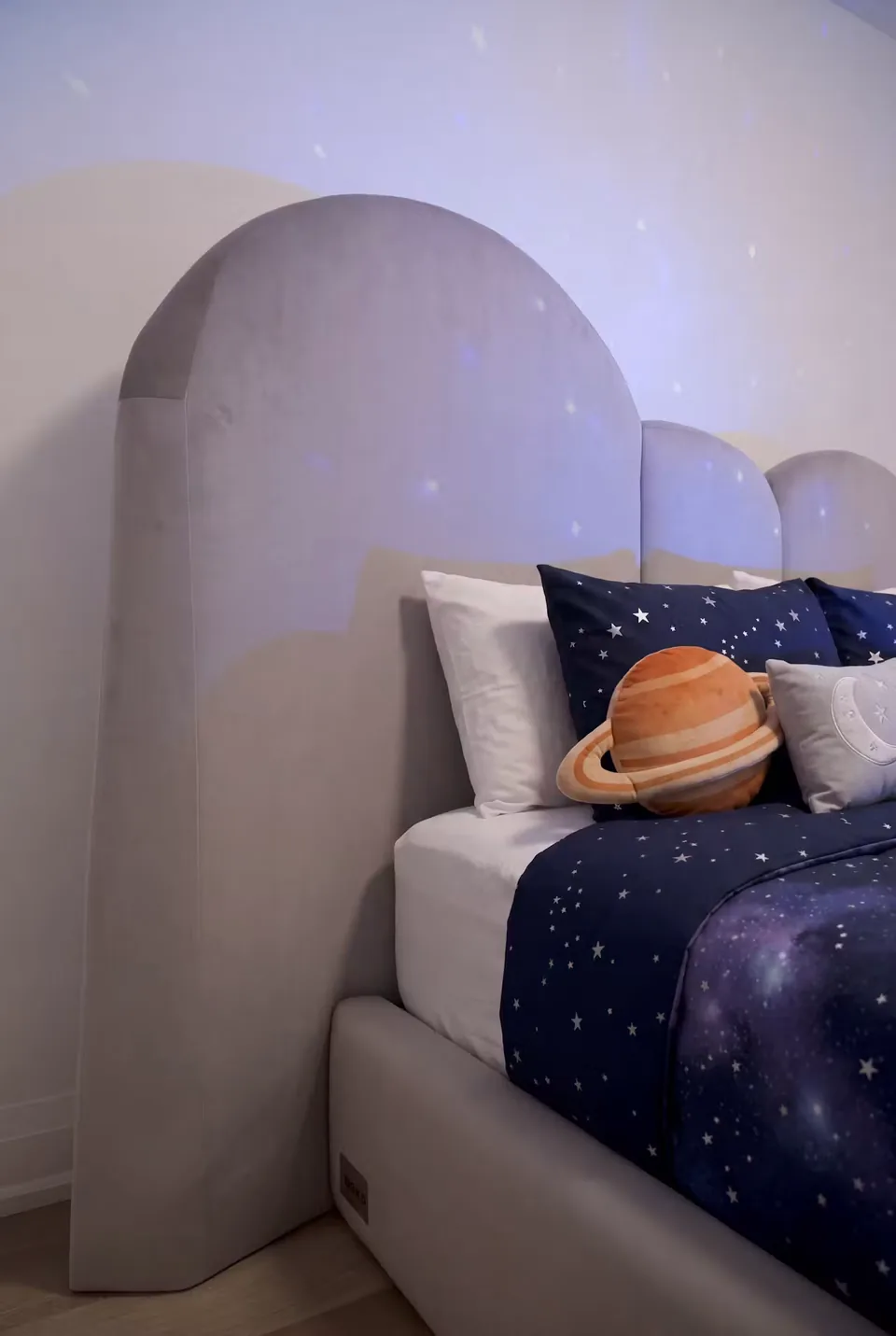 Close view of the curved grey headboard behind the patterned pillows