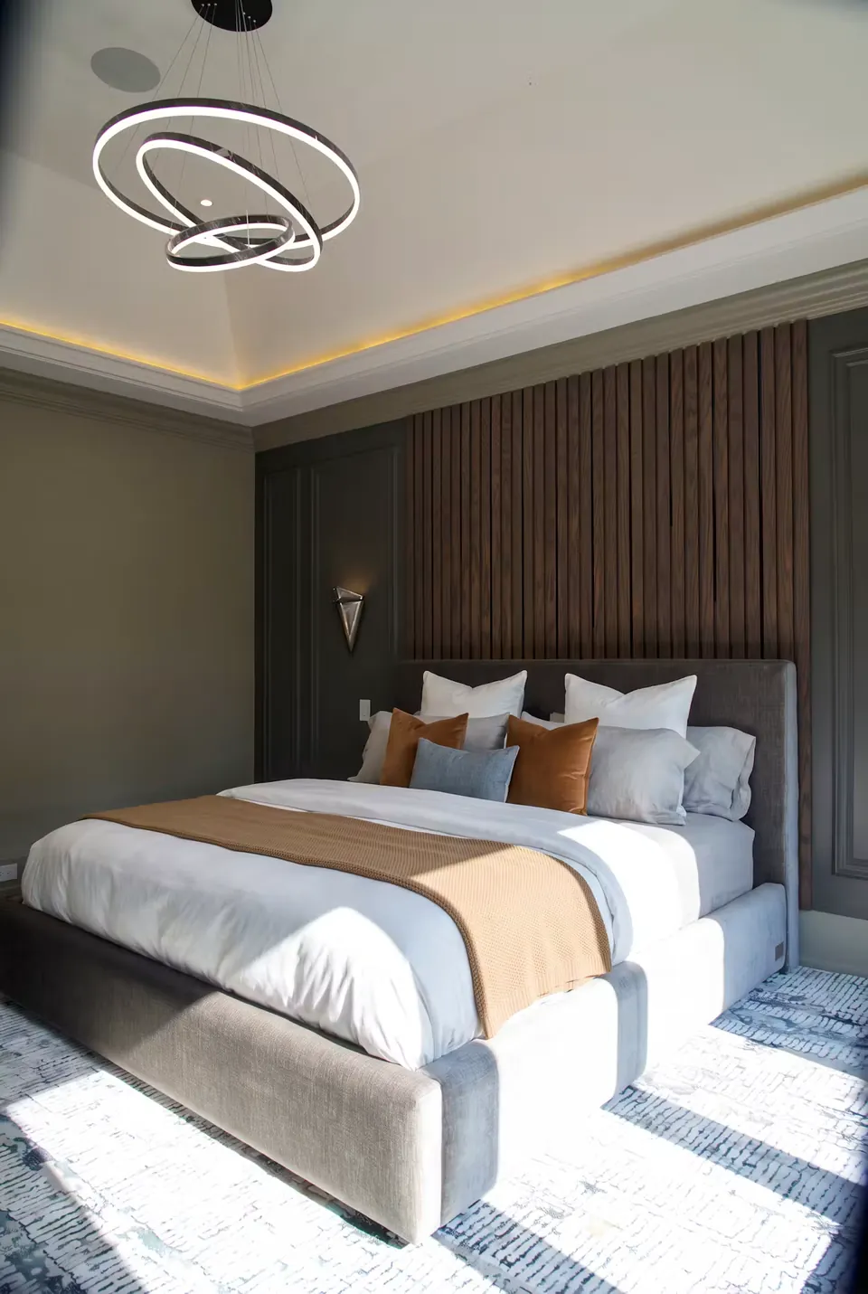 Opposite angled view of the grey bed with rust pillows and sunlight on the rug.