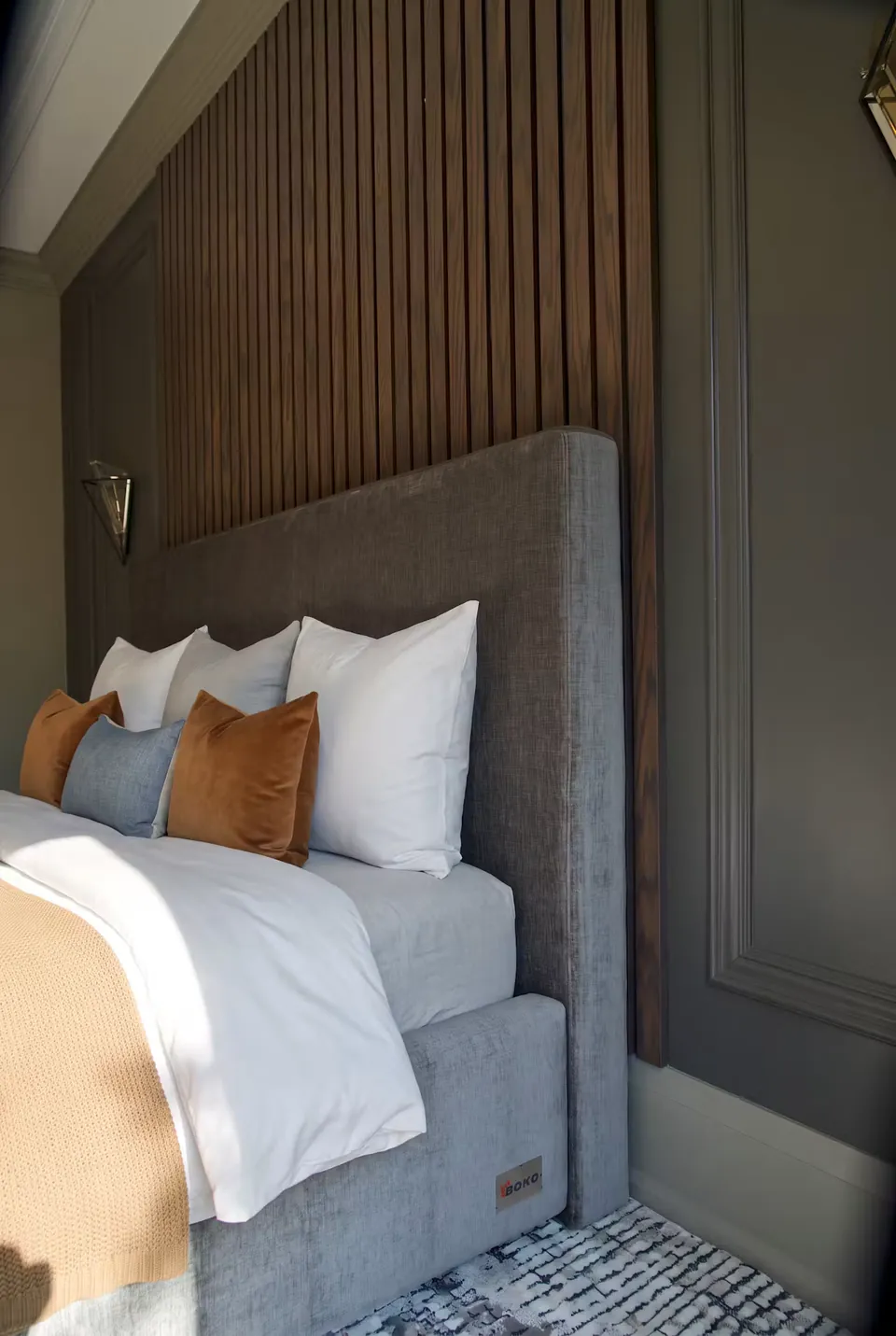 Close side view of the grey padded headboard beneath vertical wood-toned slats.