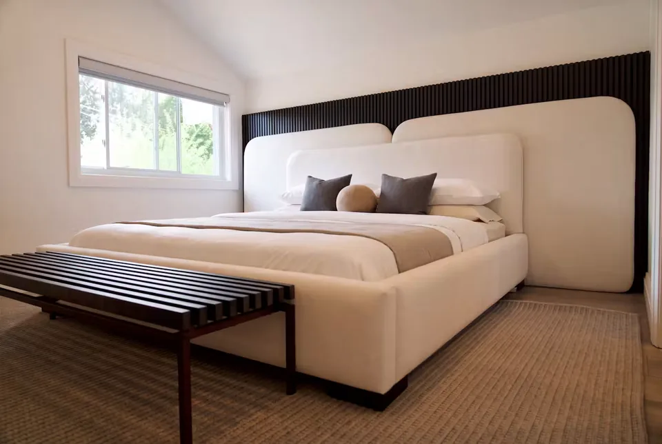 Low ivory upholstered bed and divided headboard against a lit black slatted wall