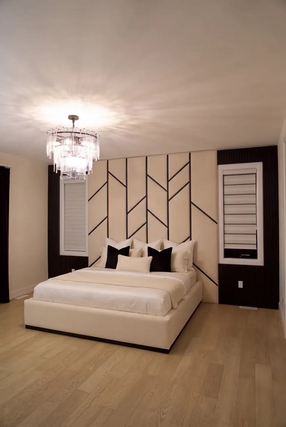 Ivory upholstered bed below a tall wall of black branching lines and a glass chandelier