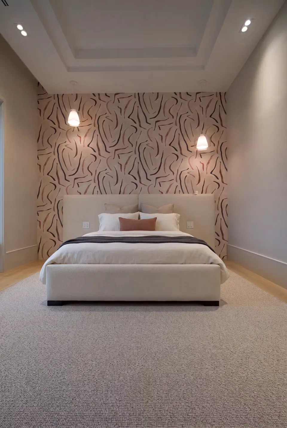 Full ivory upholstered bed with a lightly buttoned headboard against leaf-patterned wallpaper