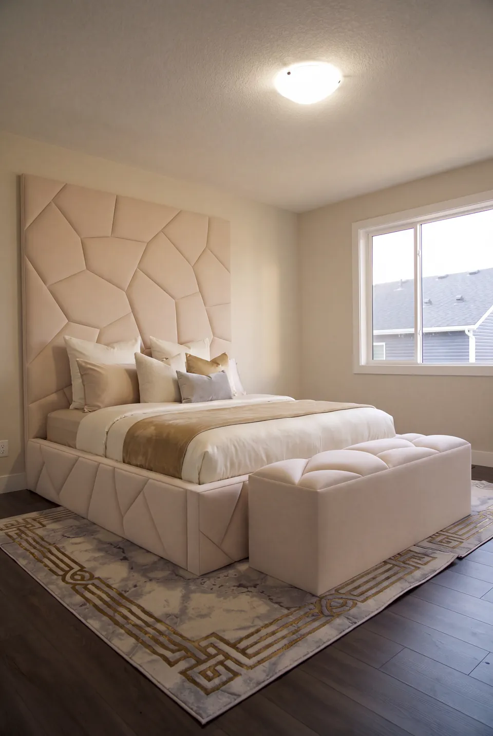 Full view of an ivory geometric upholstered bed with a matching bench and faceted wall panels.