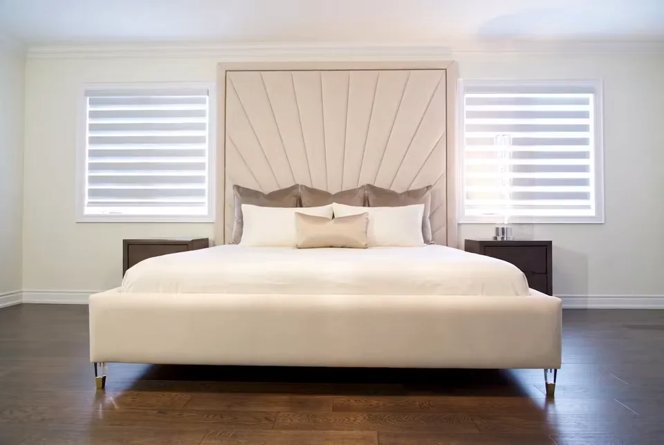 Full ivory bed with a framed fan headboard between two shuttered windows