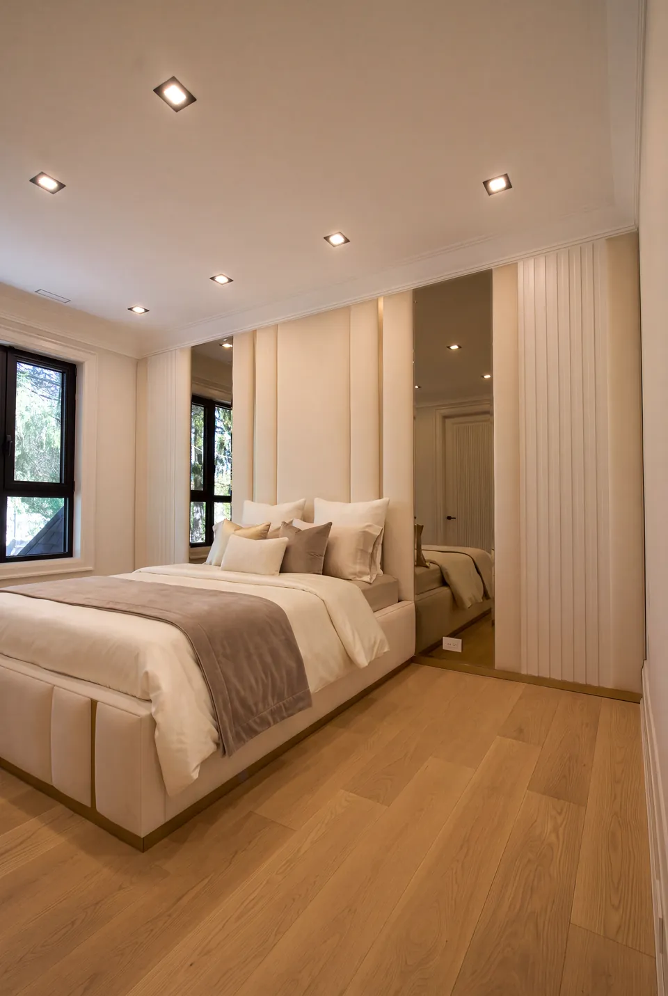 Angled full view of the ivory bed beneath mirrored and upholstered wall sections.