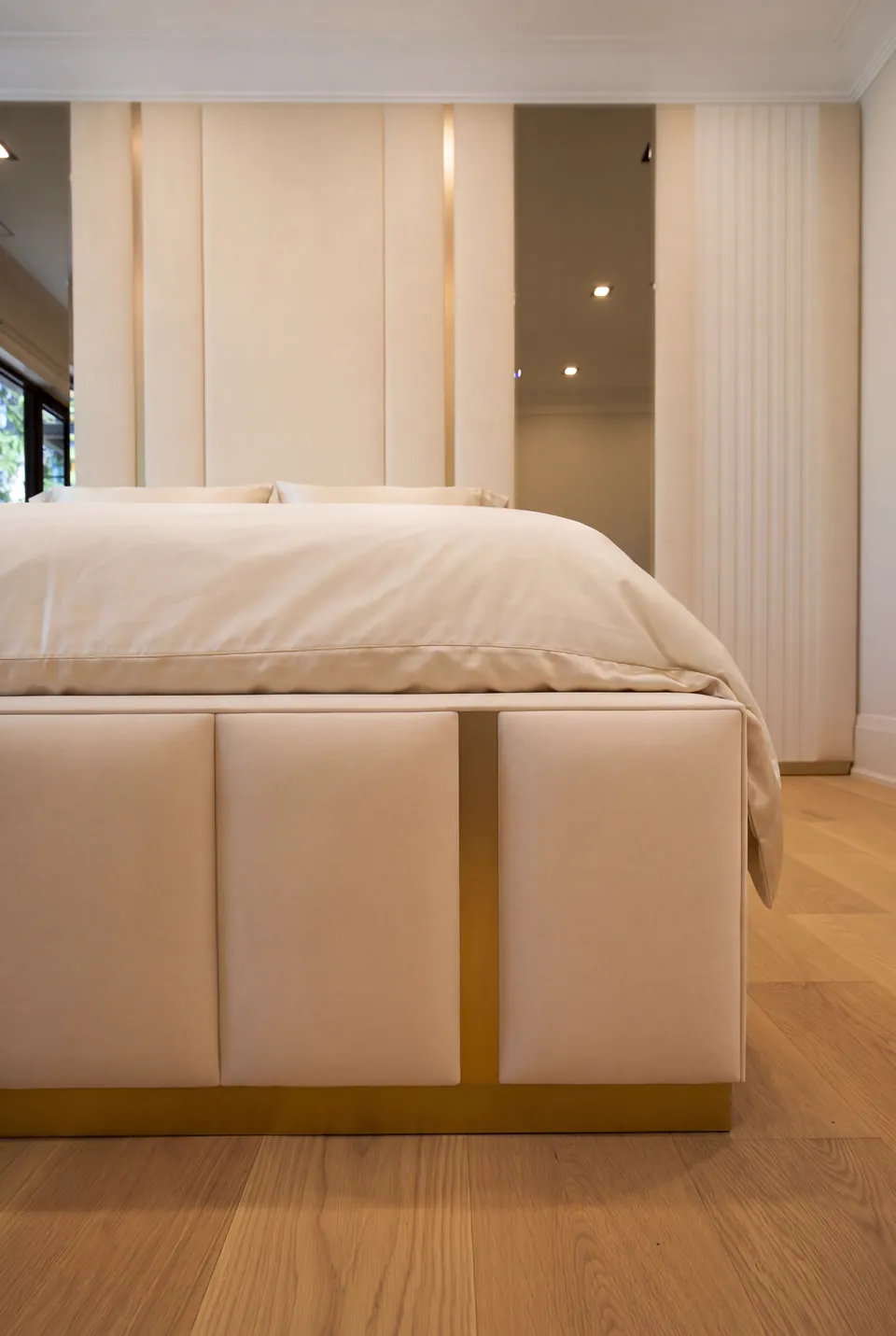 Detail of an ivory padded footboard section with gold-toned trim.