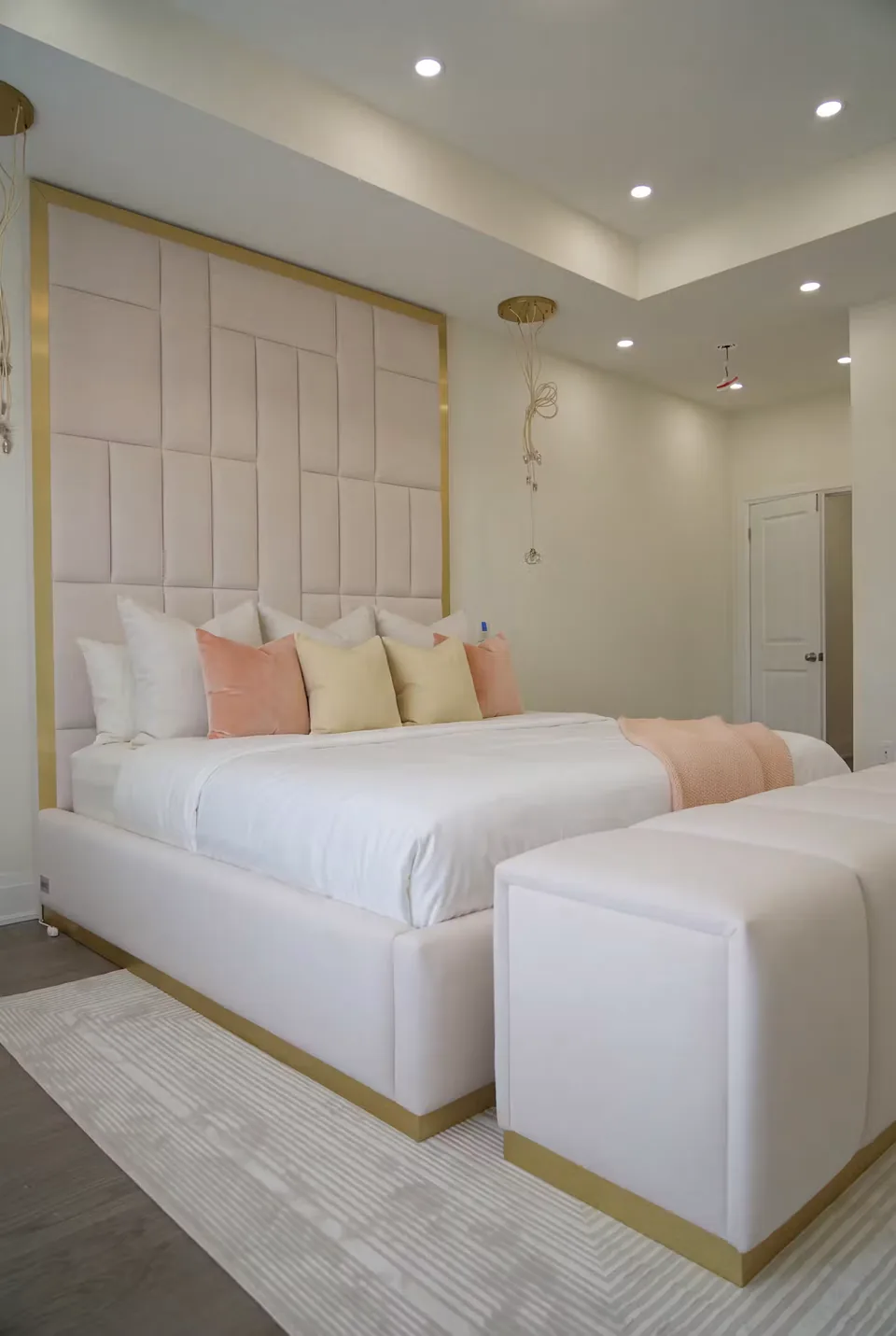 Wide view of an ivory upholstered bed and gold-trimmed bench below rectangular wall panels