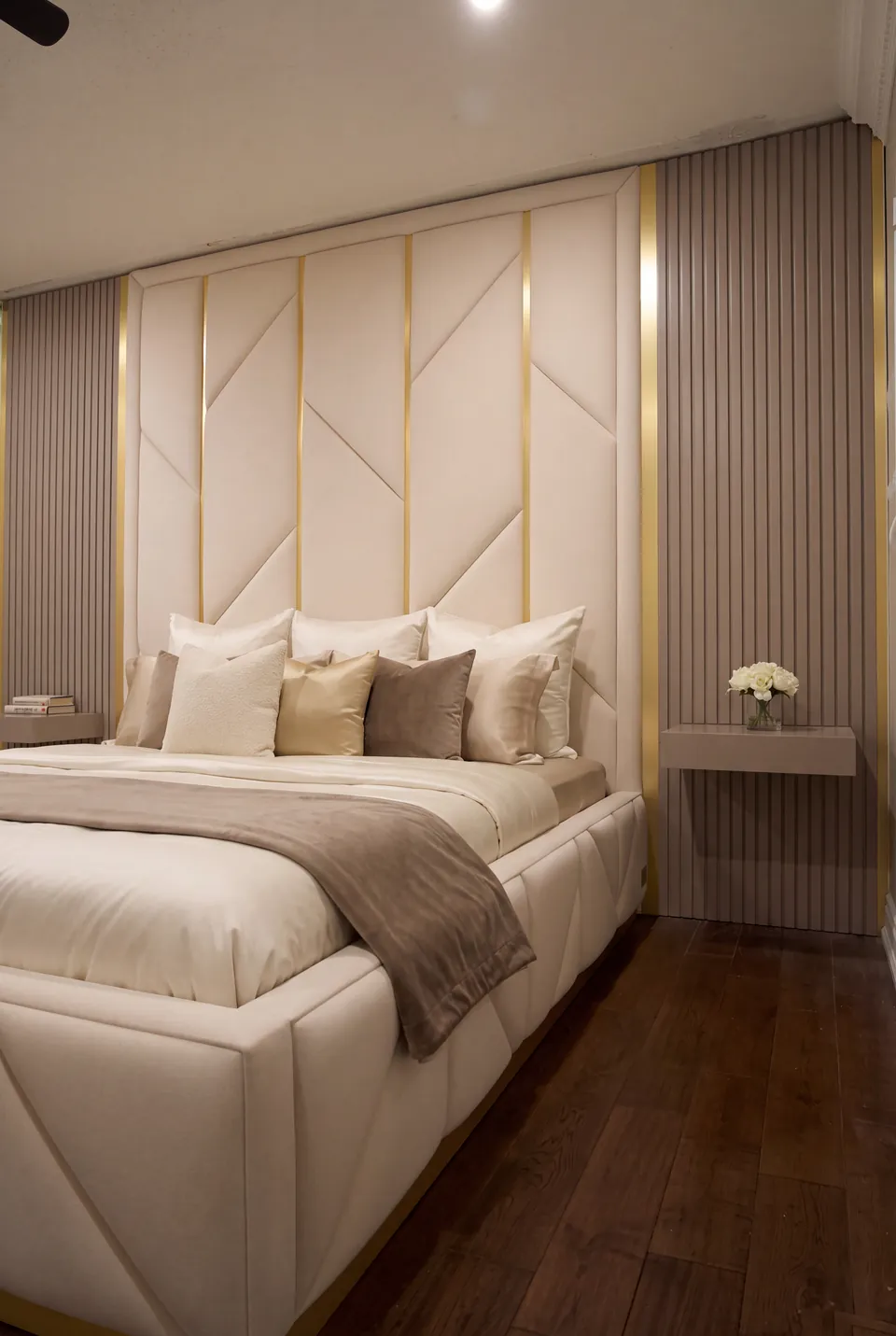 Wide angled view of an ivory bed with faceted side panels beneath a gold-divided upholstered wall.