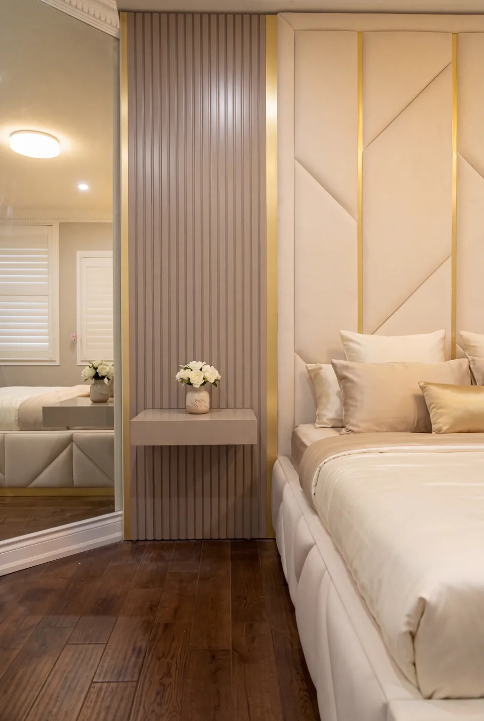 View of an ivory headboard beside grey vertical slats, a mirror and a floating bedside drawer.