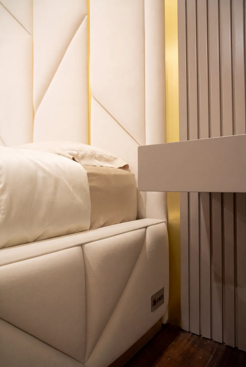 Close view of diagonal seams on the ivory upholstered bed frame beside grey wall slats.
