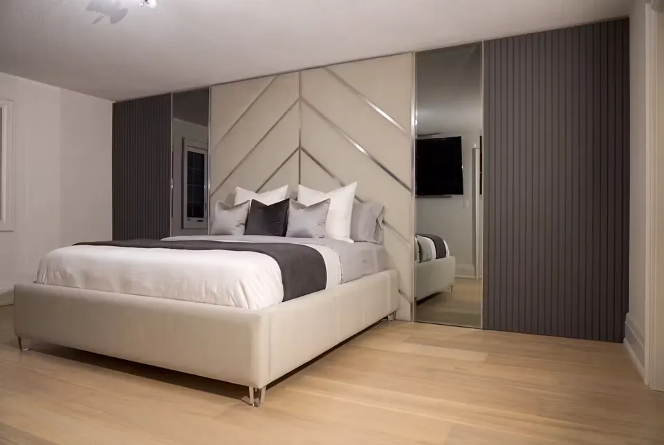Full wide view of an ivory bed beneath chevron wall panels with tall mirrors at the sides.