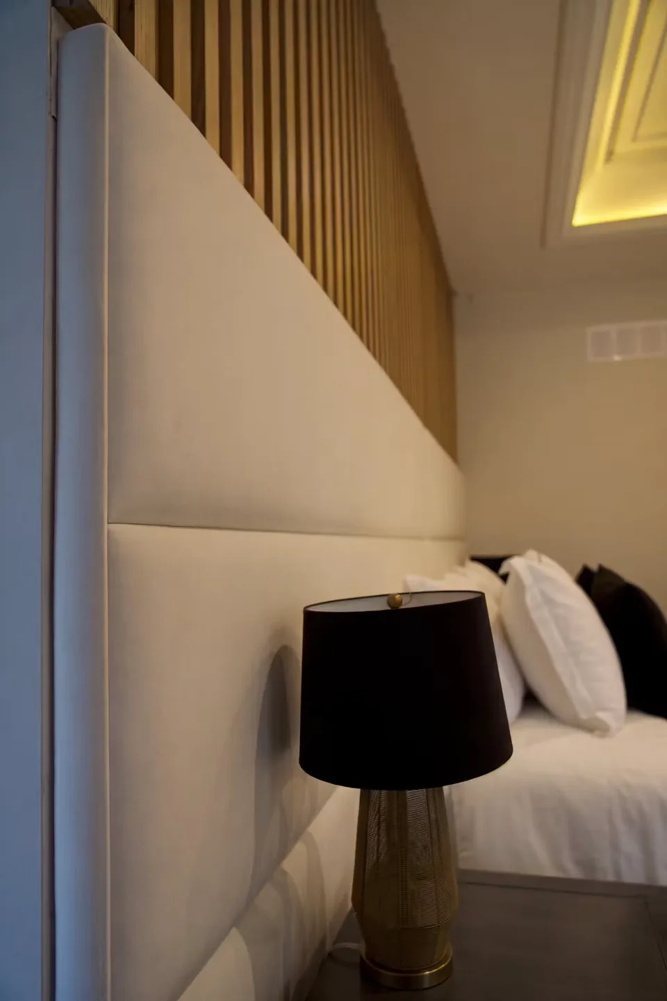 Detail of the ivory headboard beside a black lamp and vertical slats