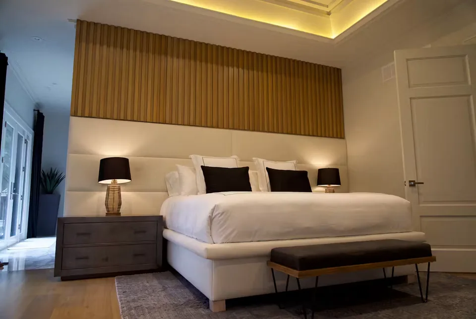 Angled room view of the pale bed beneath the warm slatted band