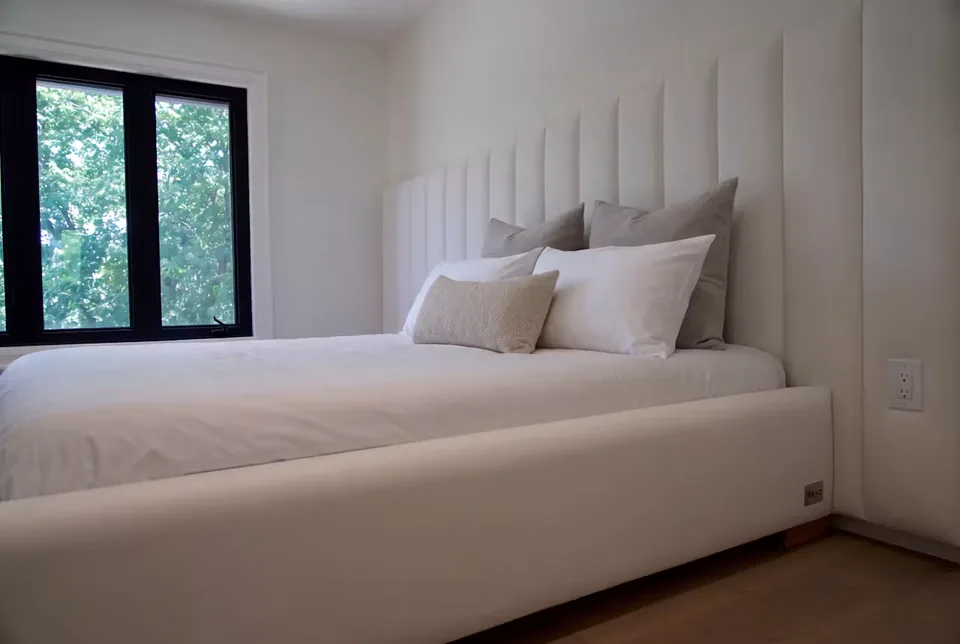 Angled view of the ivory upholstered bed with a channelled wall
