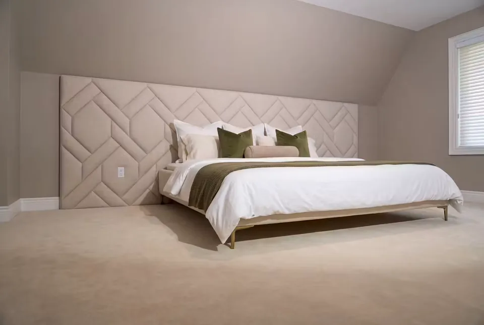 Full wide view of an ivory upholstered bed and woven diagonal padded wall with olive cushions.