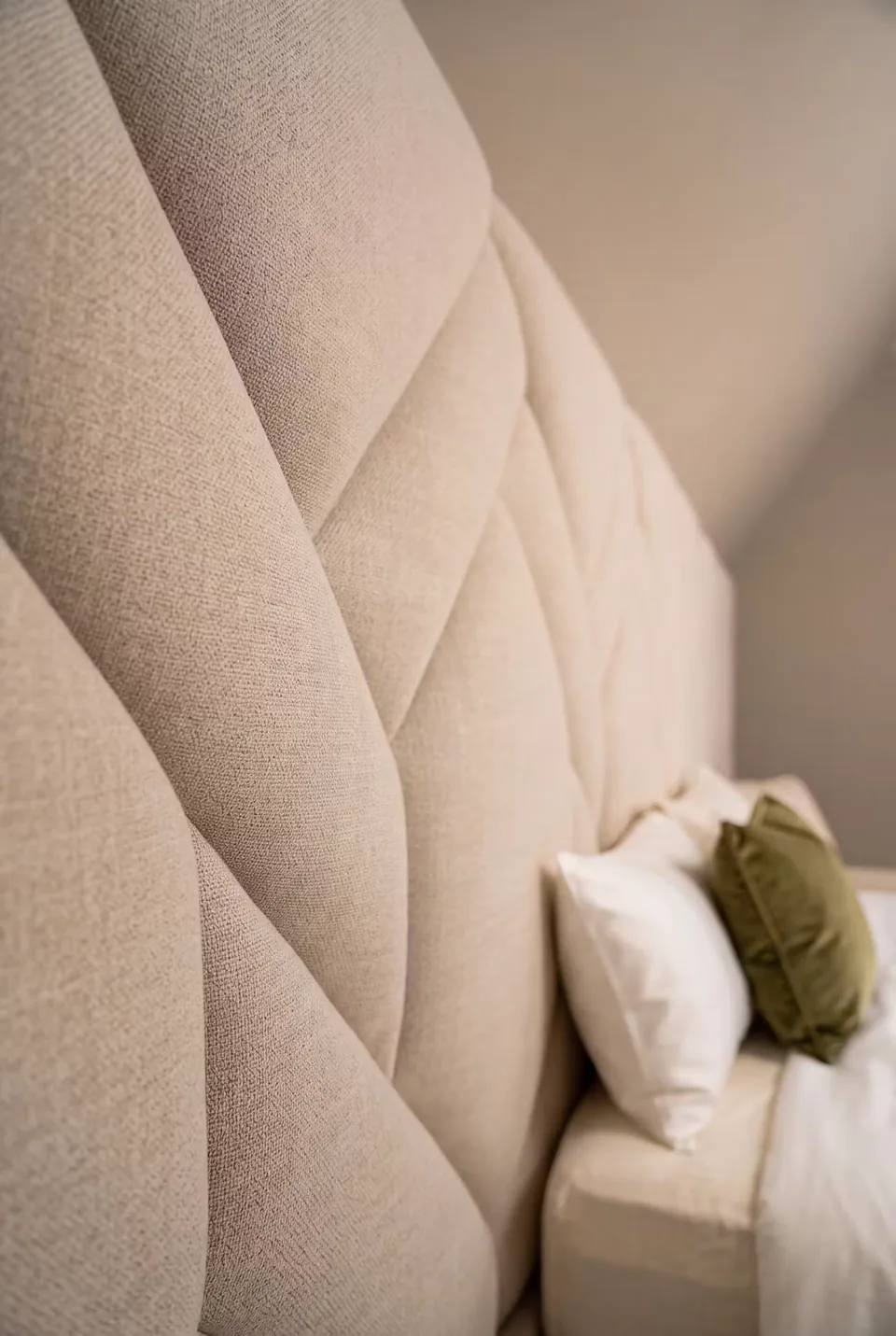 Close view of crossed ivory upholstered strips and olive cushions beside the headboard.