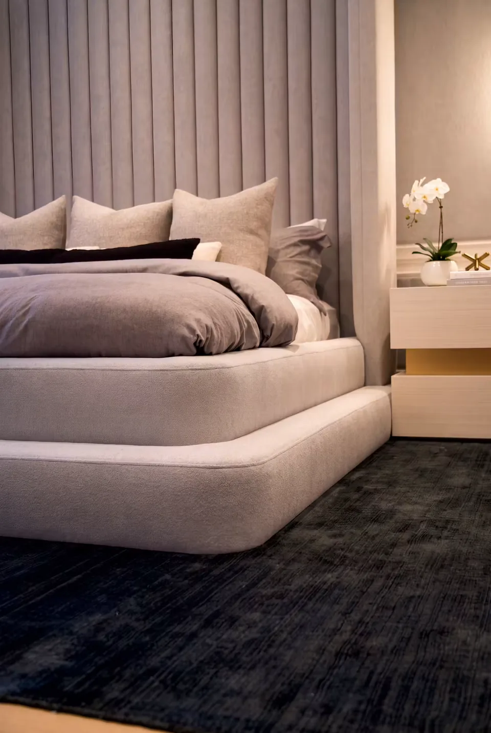 Angled view of the rounded grey bed frame and its extended upholstered platform