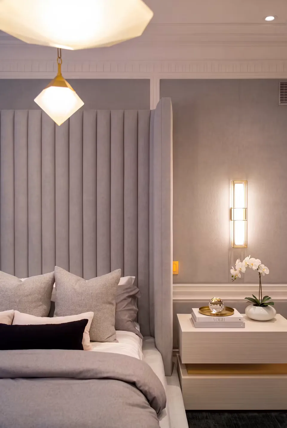 Grey headboard channels below a geometric pendant beside a floating bedside unit