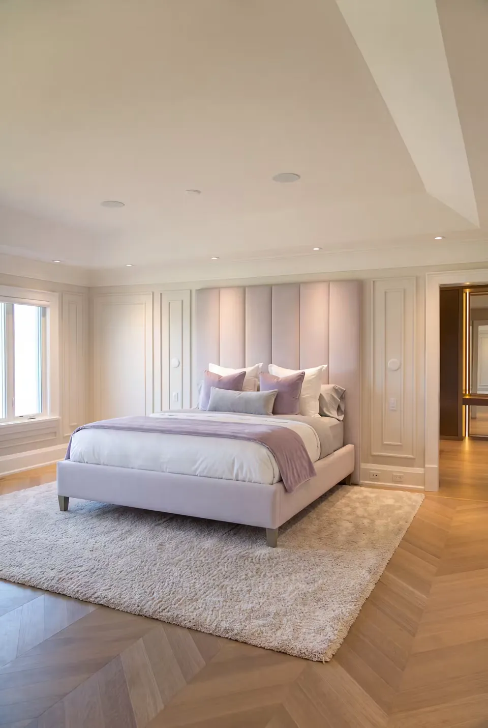 Full angled view of a pale lilac upholstered bed and tall panels within white wall mouldings.