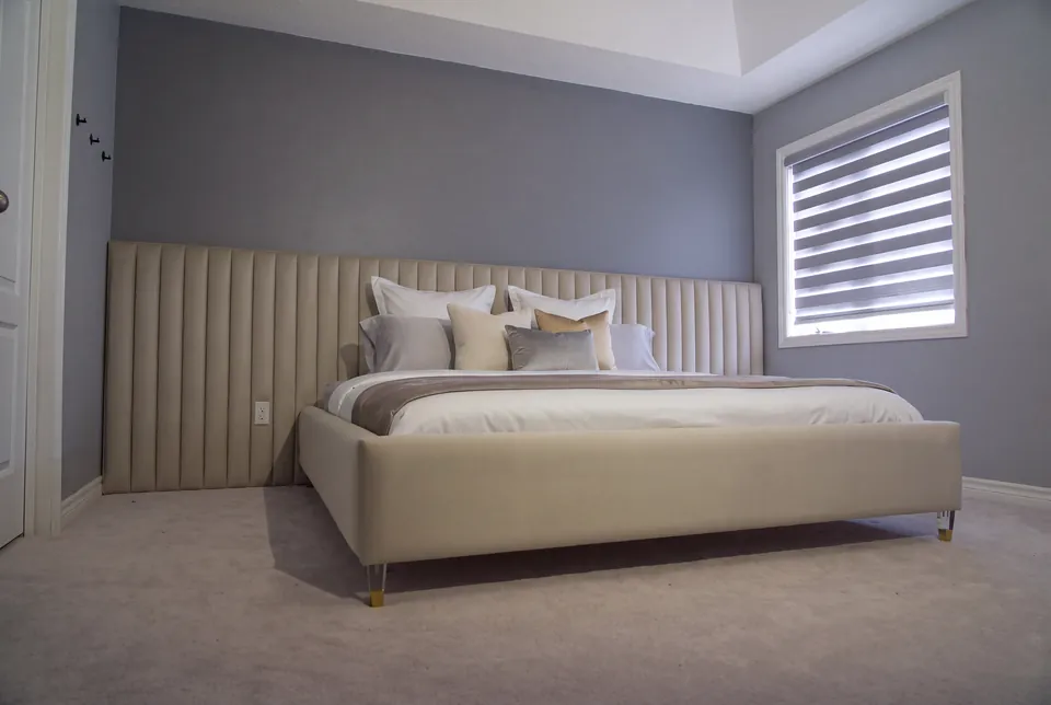 Full view of an ivory upholstered bed with a low channelled wall beneath a shuttered window.
