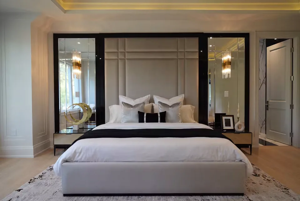 Front view of a pale upholstered bed below a padded grid between two mirrors
