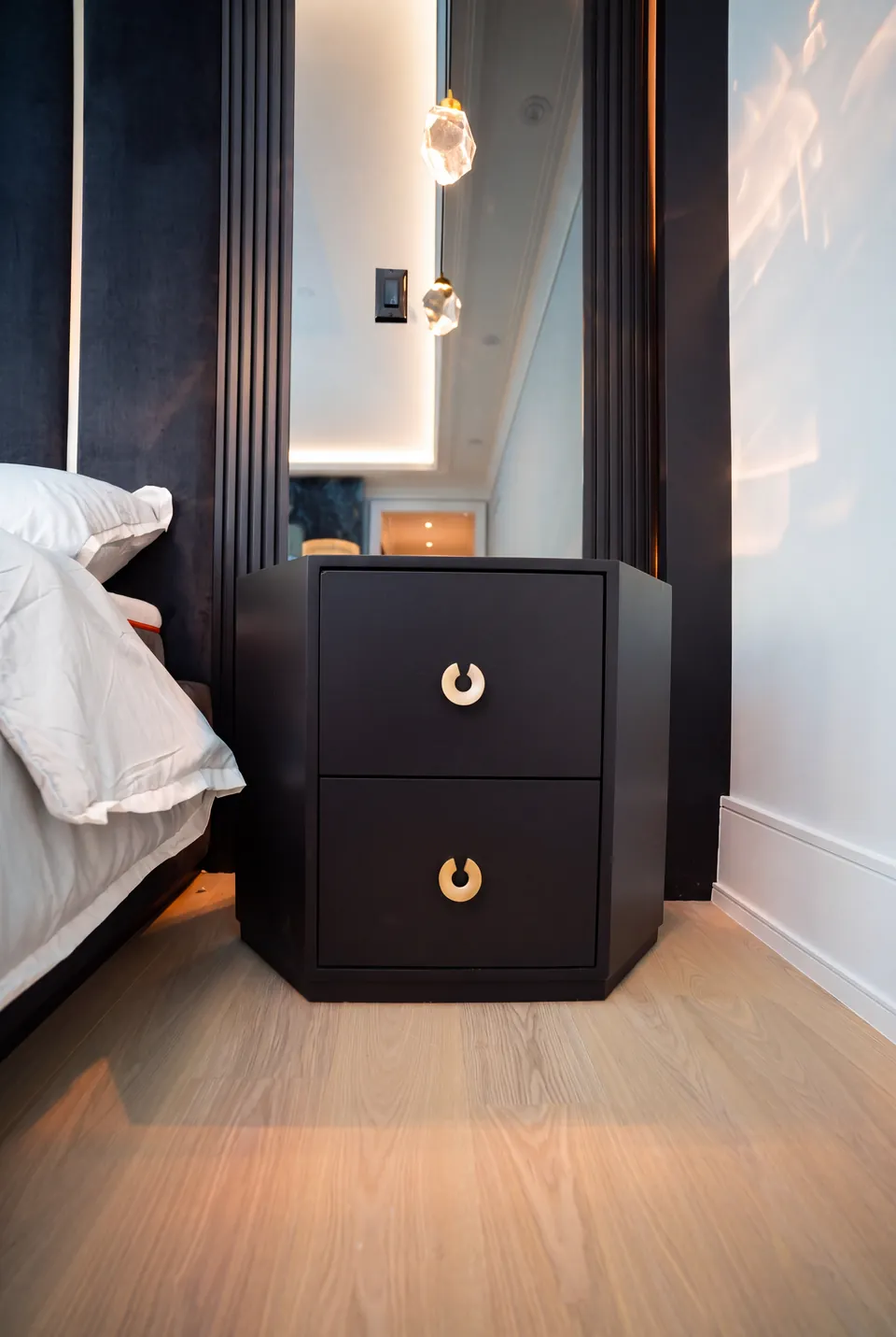 Detail of a dark bedside table with gold ring pulls next to navy upholstery.