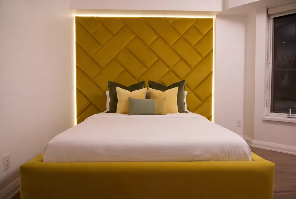 Wide front view of the ochre bed beneath the lit woven headboard