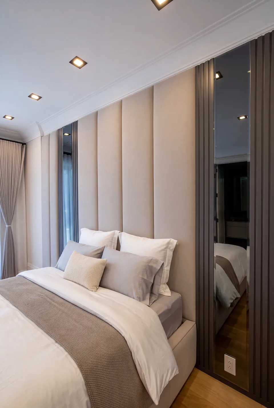 Angled view of pale vertical headboard panels reflected in a broad bedside mirror.