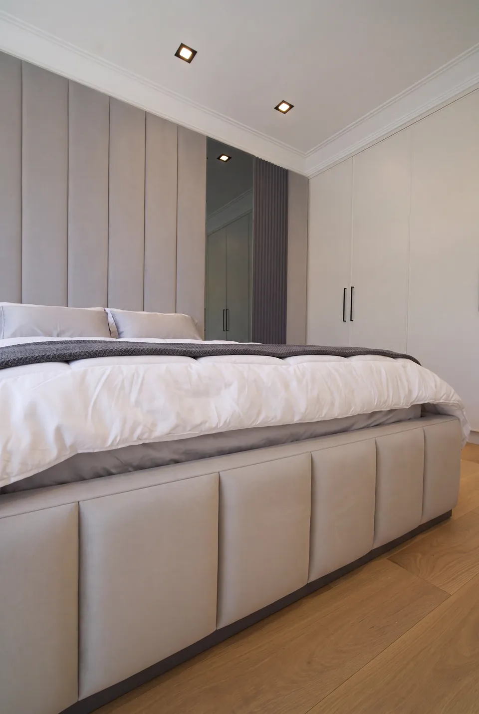 Low view of divided pale upholstered panels along the bed frame above the timber floor.