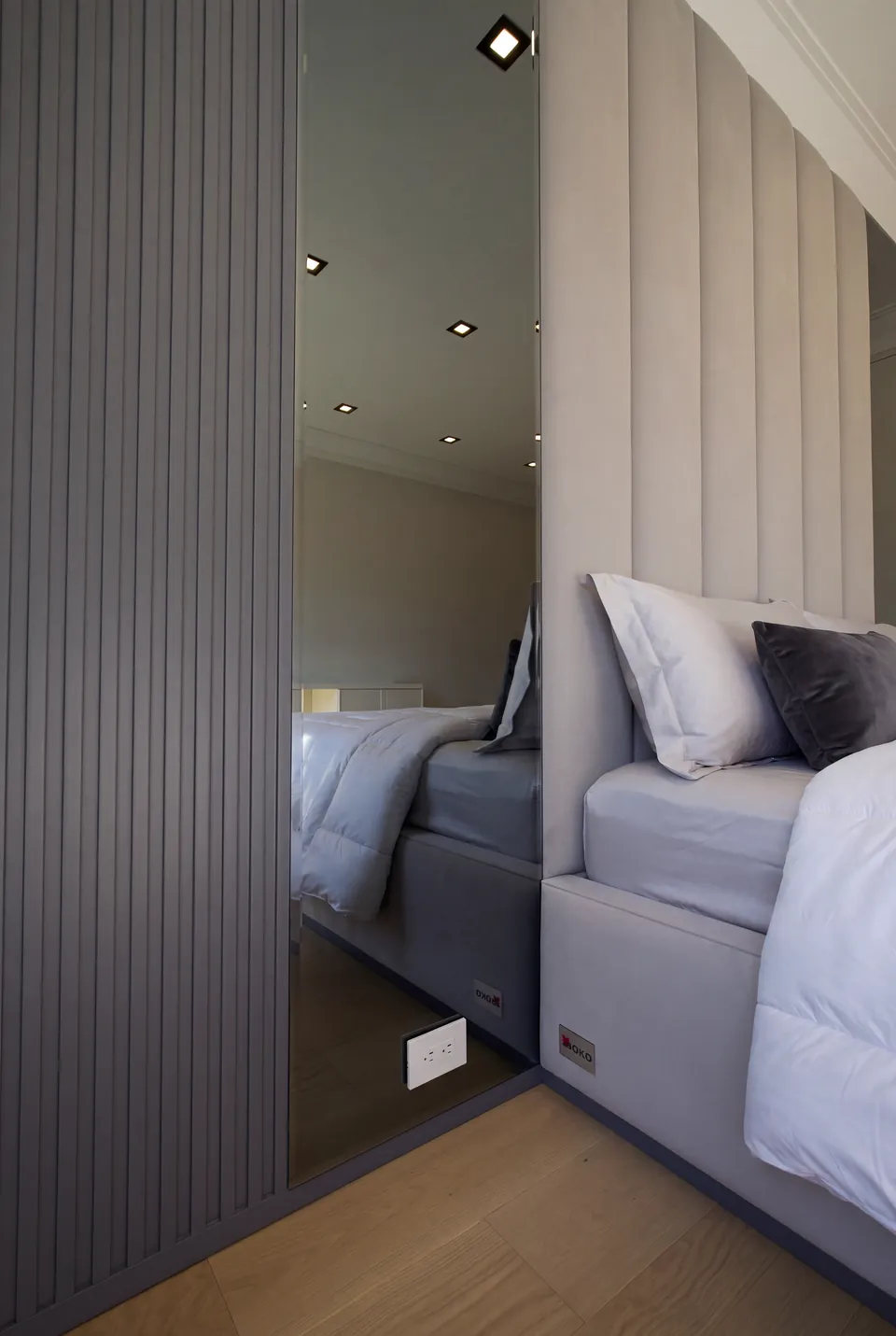 Side detail of a pale upholstered headboard beside a mirror and dark fluted wall strips.