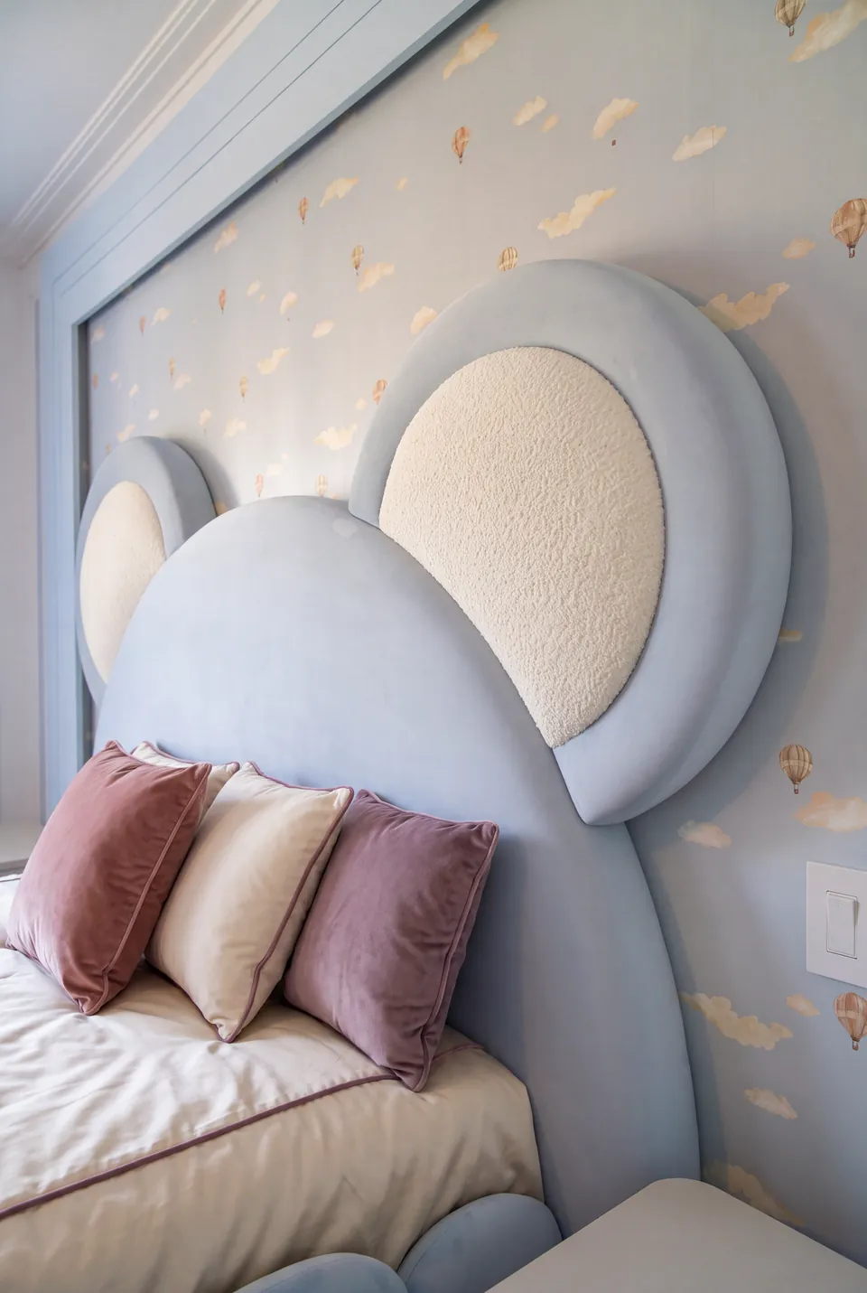Detail of the bear-shaped headboard with pale inset ears and rose cushions.