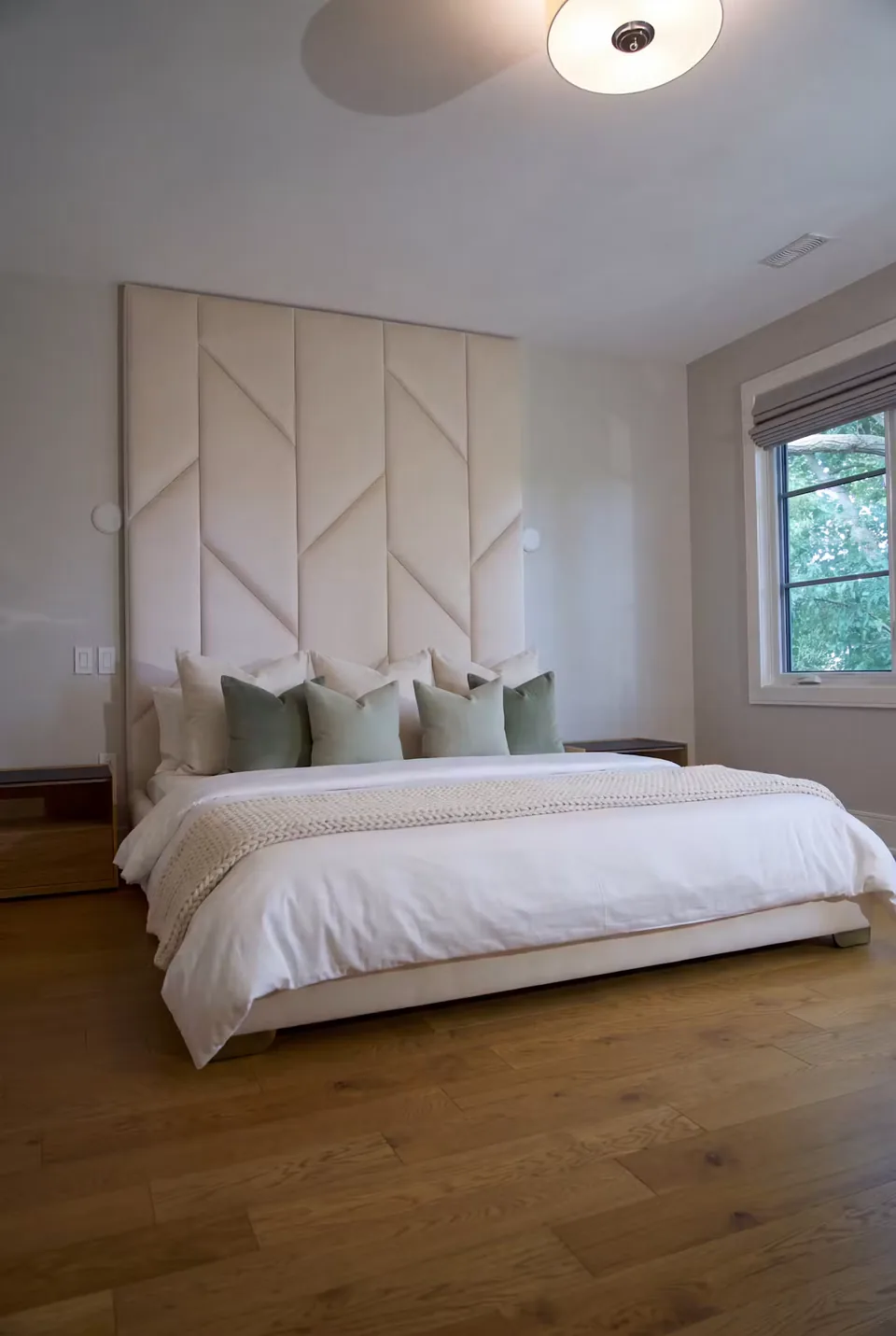 Bespoke sand-coloured bed and tall angled upholstered wall with green cushions