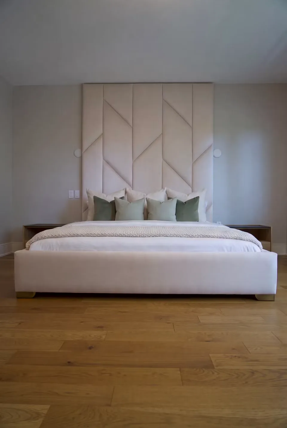 Front view of a sand-coloured bed below padded wall panels with alternating angled seams