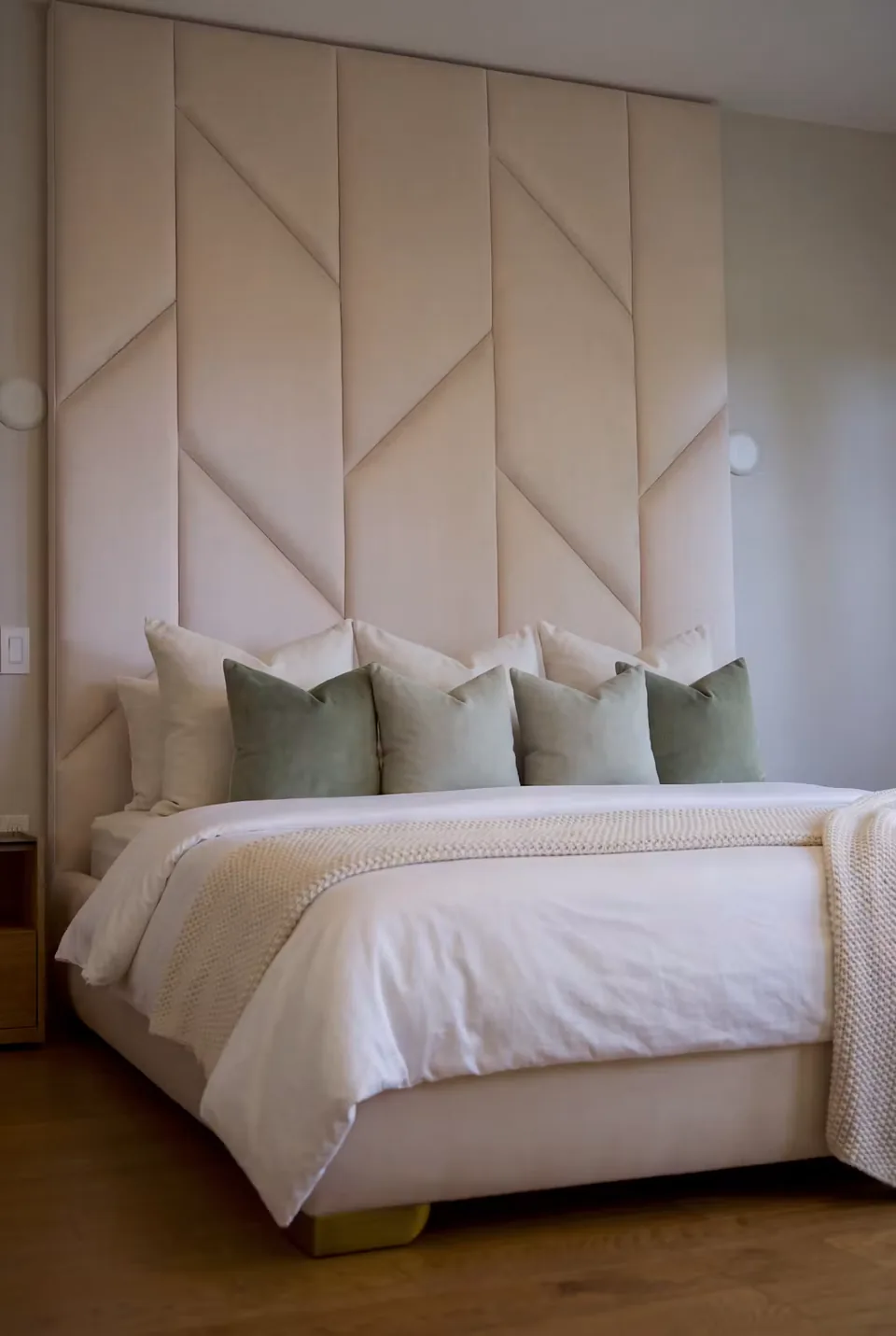 Angled view of a pale upholstered bed frame and narrow gold-toned base trim