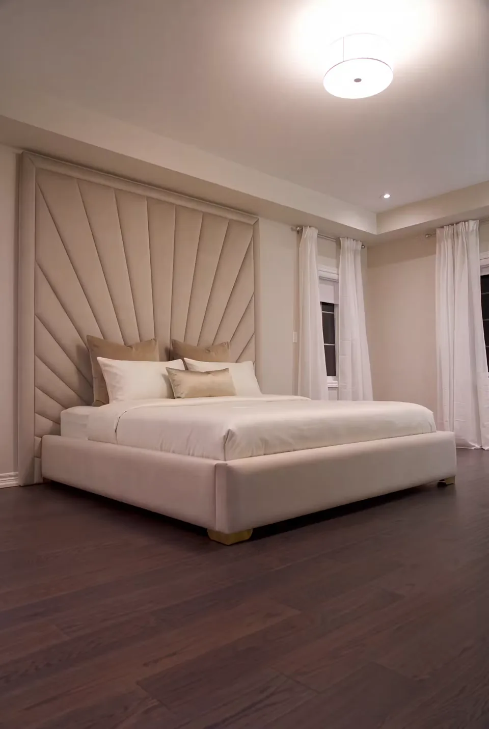 Full sand upholstered bed with a bordered fan headboard beside pale curtains
