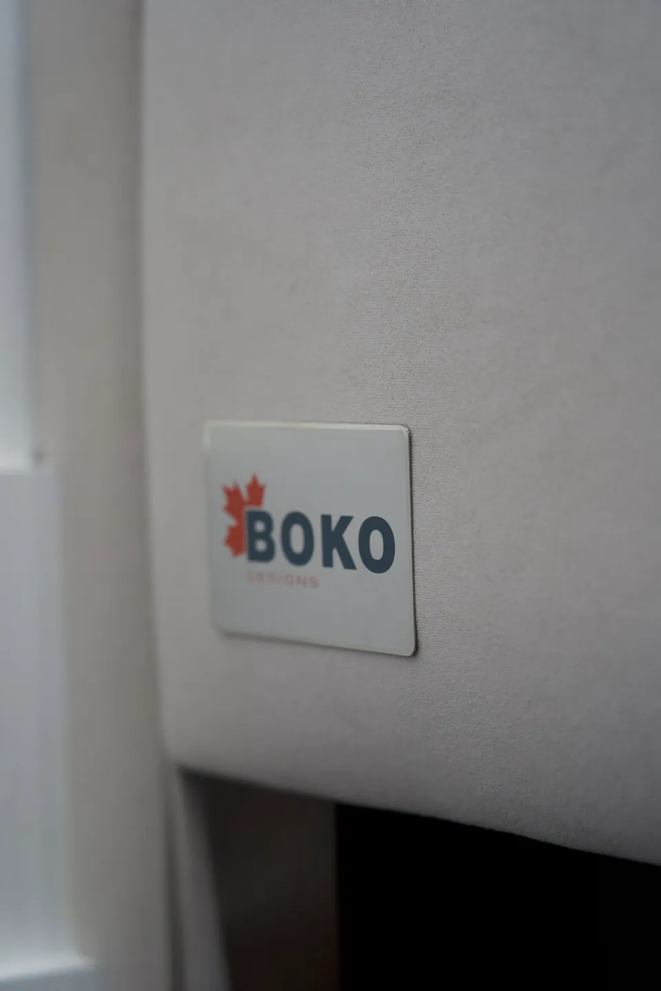 Close view of the BOKO label on the pale upholstered bed frame.