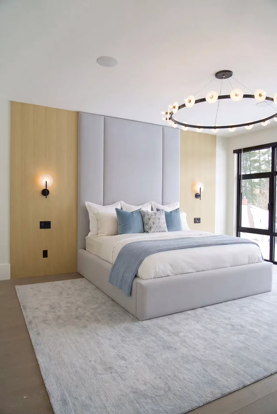 Full angled view of a silver-grey upholstered bed beneath broad padded columns and gold divisions.
