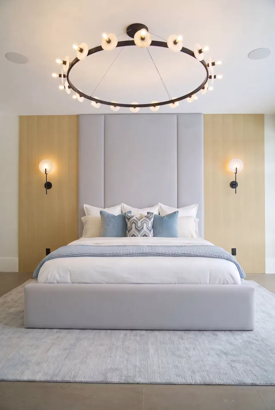Full front view of the low grey bed with a tall panelled headboard and pale blue cushions.