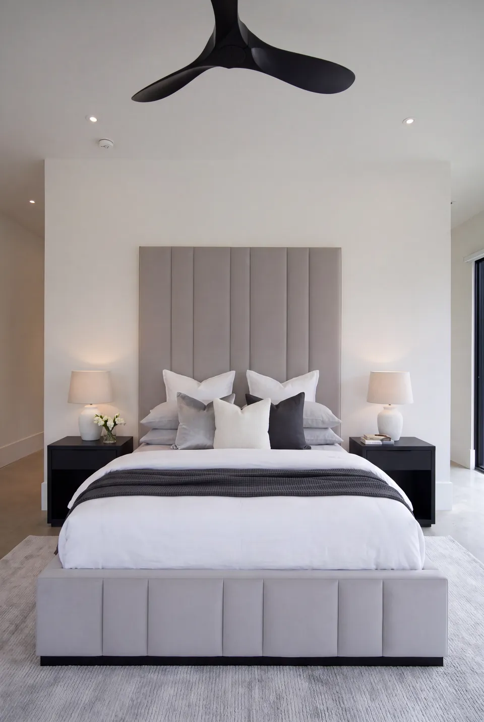 Front view of a silver-grey channel bed between black bedside tables.