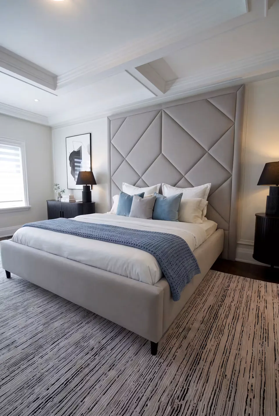 Silver-grey upholstered bed with a tall bordered diamond headboard and blue cushions