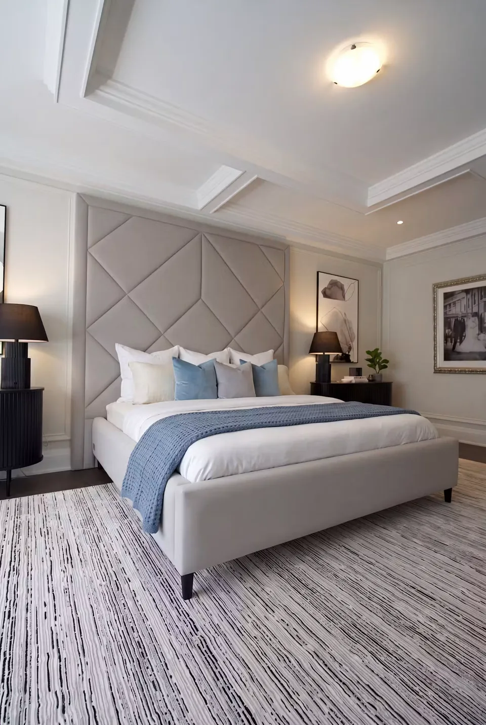 Angled view of a grey bed and geometric headboard between dark bedside tables