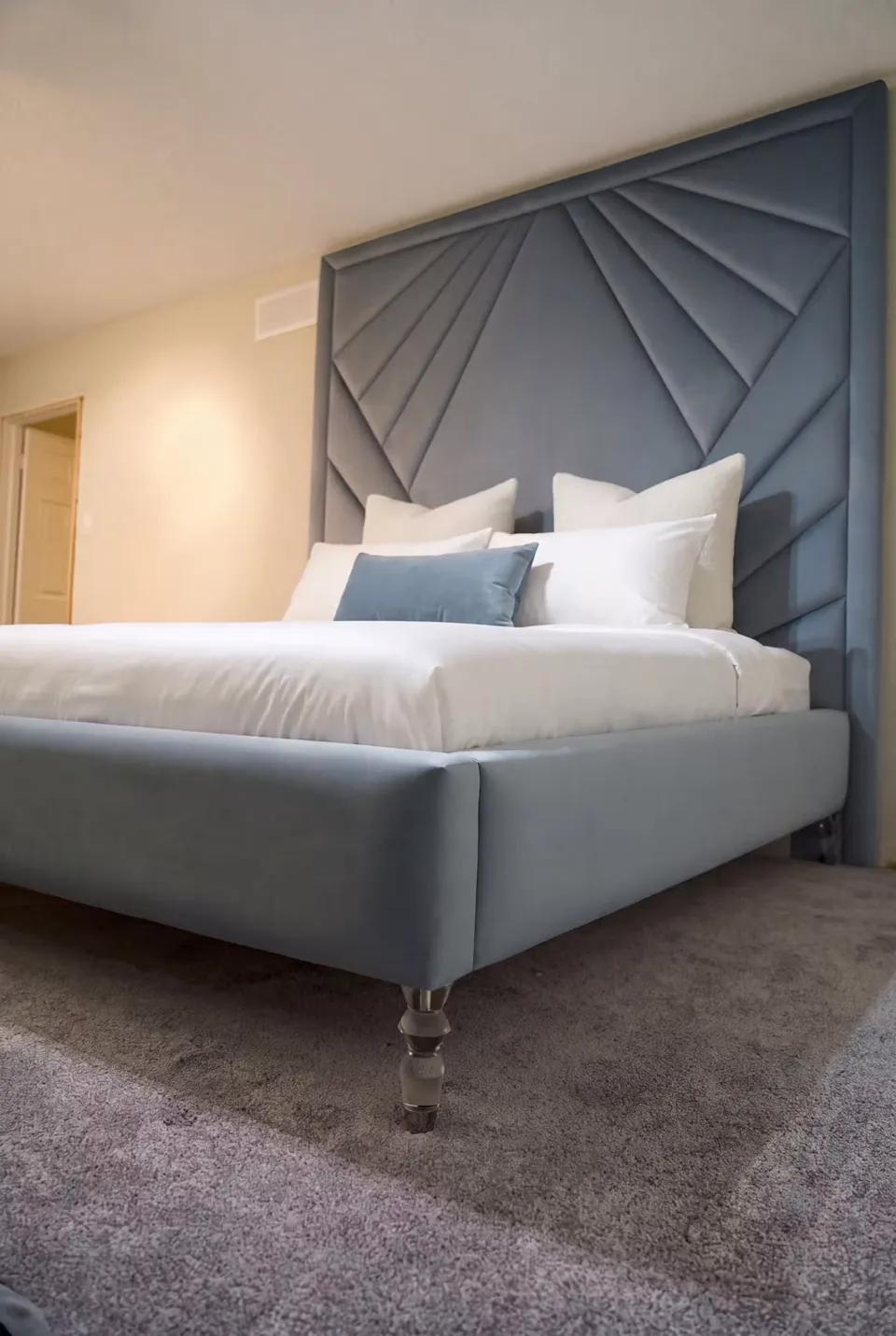Slate-blue upholstered bed with a bordered fan headboard and clear feet