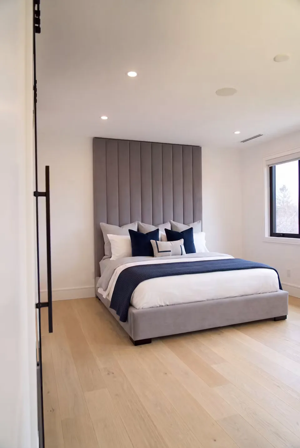Slate-grey channel headboard and upholstered bed with blue bedding on light wood flooring
