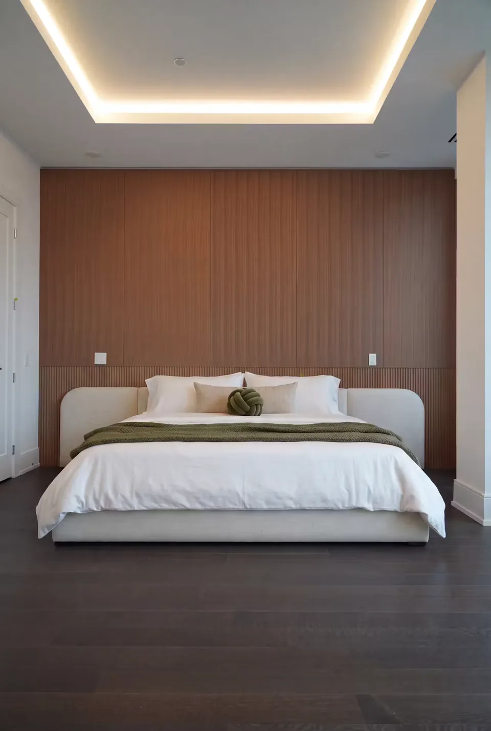 Low ivory upholstered bed with rounded headboard corners against a warm slatted wall