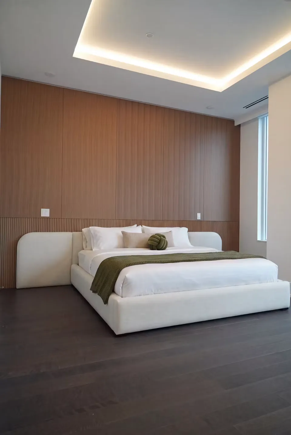Angled view of the low pale bed on a dark floor beneath vertical wall slats