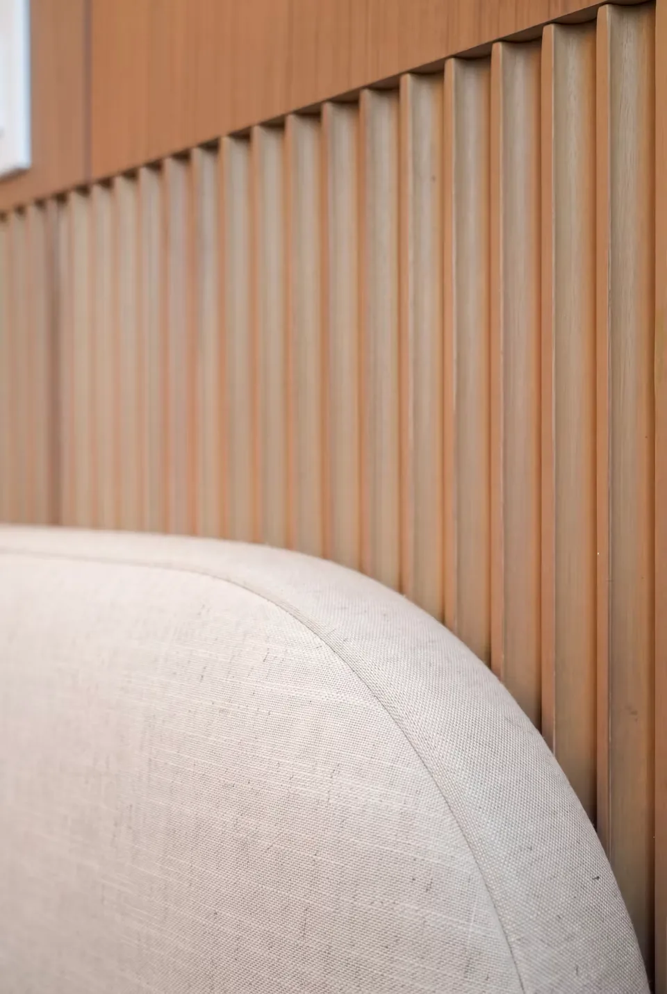 Close view of vertical wall slats behind the curved edge of an ivory headboard